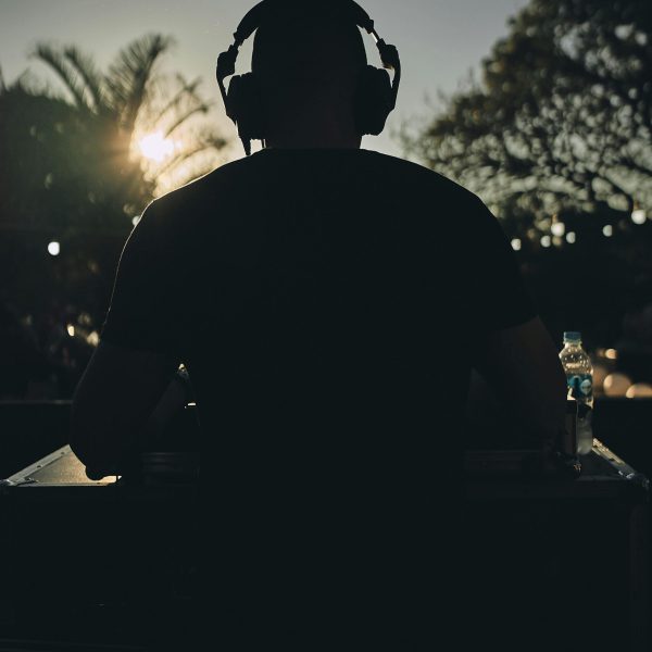 Silhouette of a DJ with headphones performing at sunset with tropical surroundings.