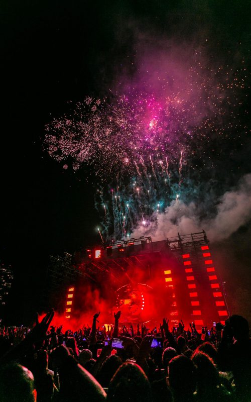 Energetic outdoor concert at night with a vibrant fireworks display and crowd enjoying live music.