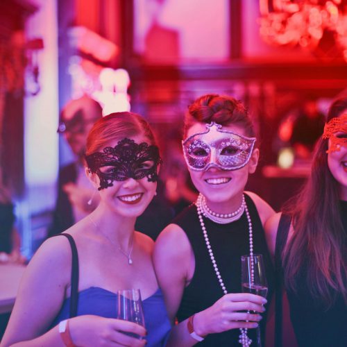 A vibrant masquerade party with happy guests wearing decorative masks and holding champagne glasses.
